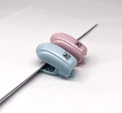 Mini staplers in pink and light blue, angled view showing staple output
