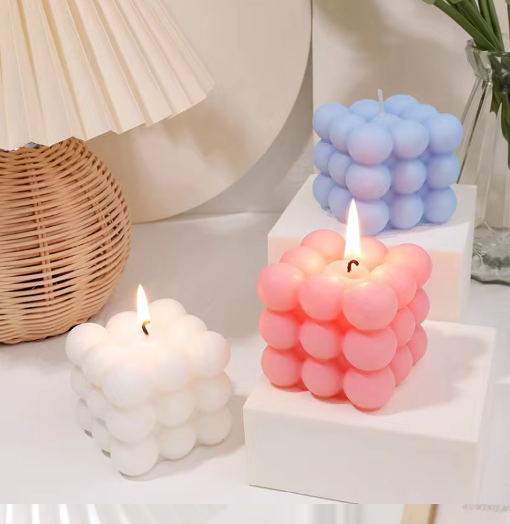 Cube candle trio in white, pink, and light blue, displayed on gift boxes
