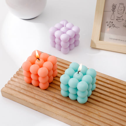 Three bubble cube scented candles with flames: lavender, coral orange, and teal blue
