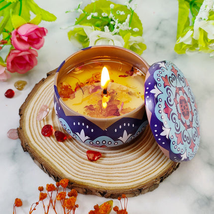 Lit vanilla scented votive candle in blue-purple patterned metal tin, lid beside