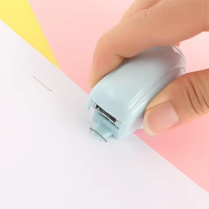 Hand using light blue mini stapler on paper, stapler tip pressing down