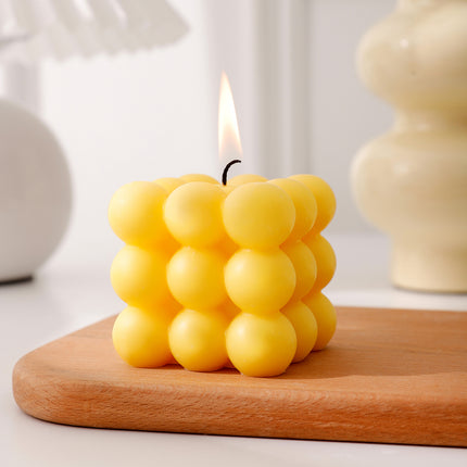 Yellow bubble cube scented candle with a small flame on a wooden surface