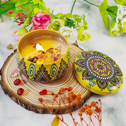 Lit soy scented candle in patterned votive tin with lid on wood slice