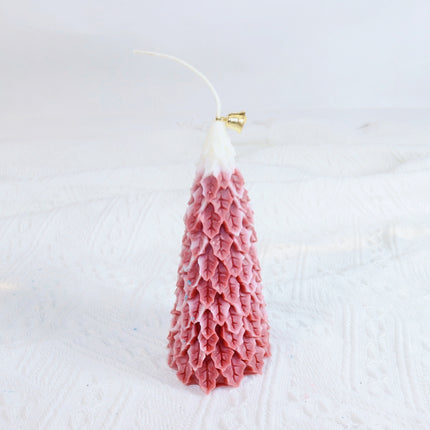 Red-pink Christmas tree candle with white wick on textured surface