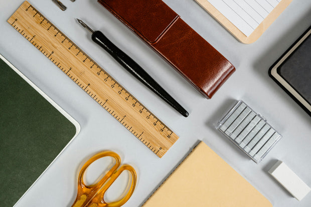 Wooden ruler, fountain pen, scissors, notebooks, and stationery supplies on a desk