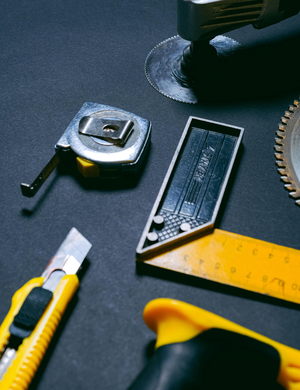 Assorted tools including tape measure, utility knife, and ruler on dark surface