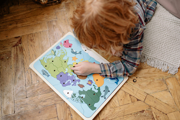 Child playing with educational world map puzzle on wooden floor